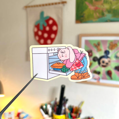 Cartoon sticker of a character baking a cake on a desk with colorful background