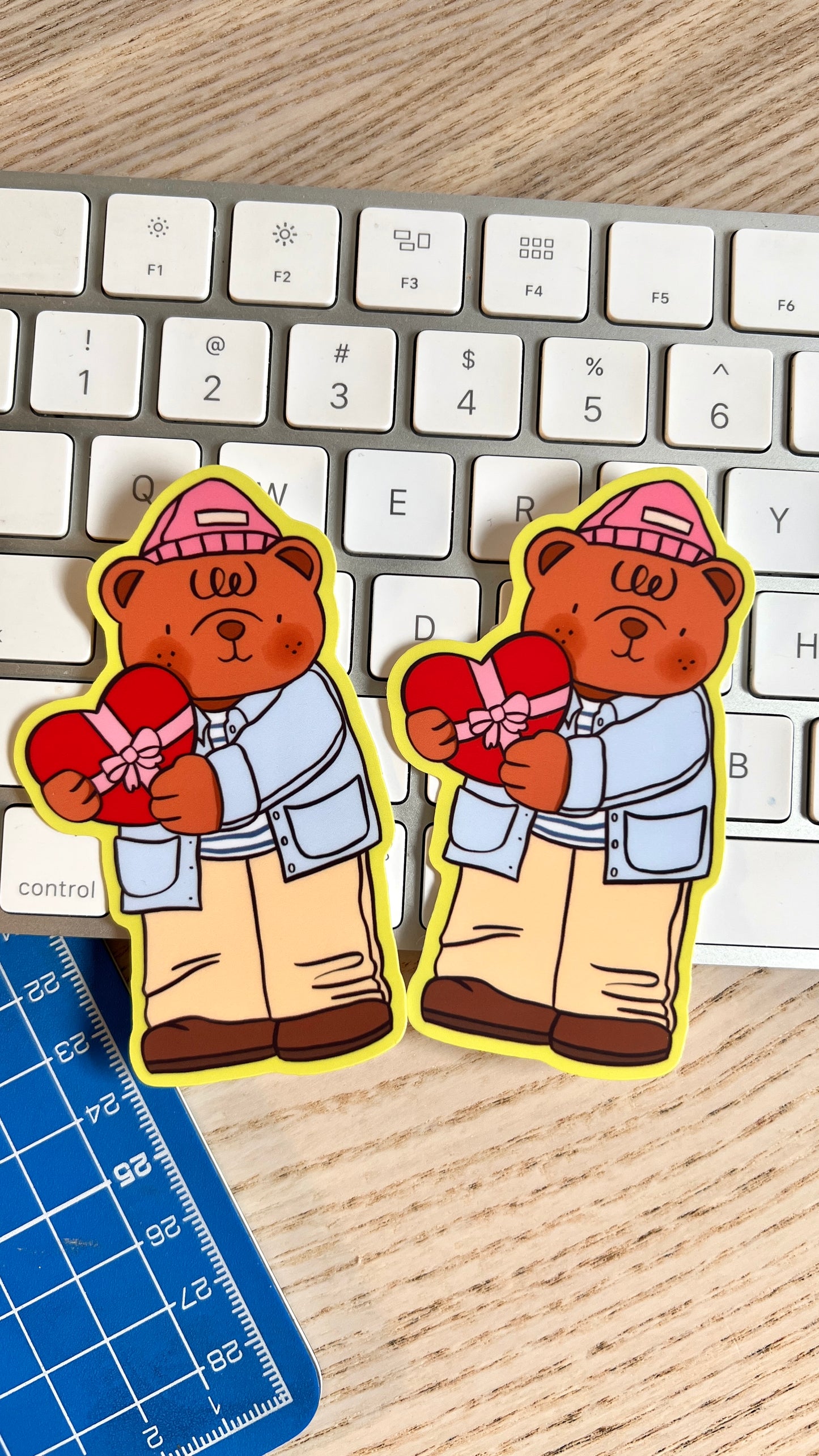 Two stickers of a bear holding a heart on a keyboard with a ruler below.