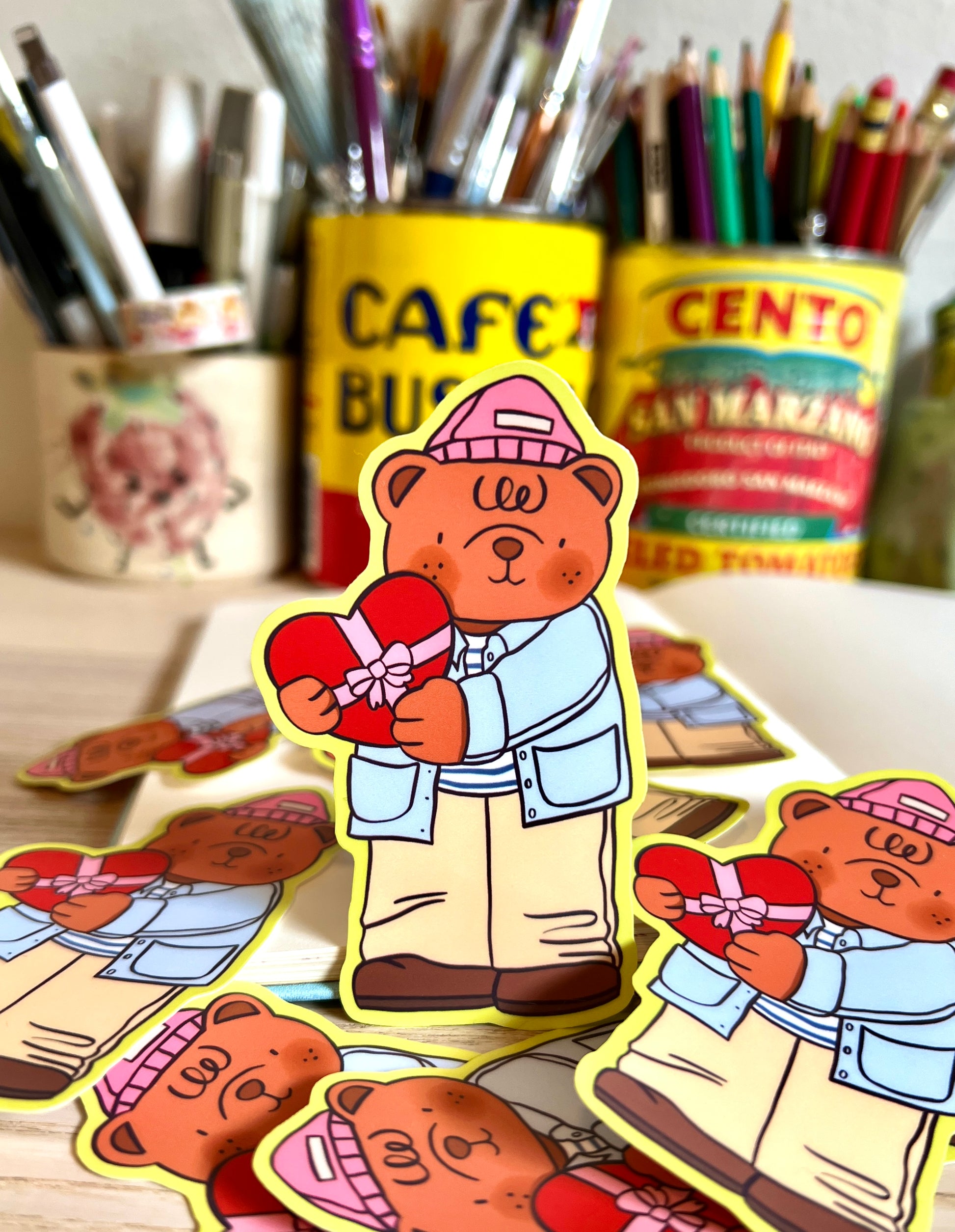Cartoon bear holding a heart-shaped gift with stationery items in the background