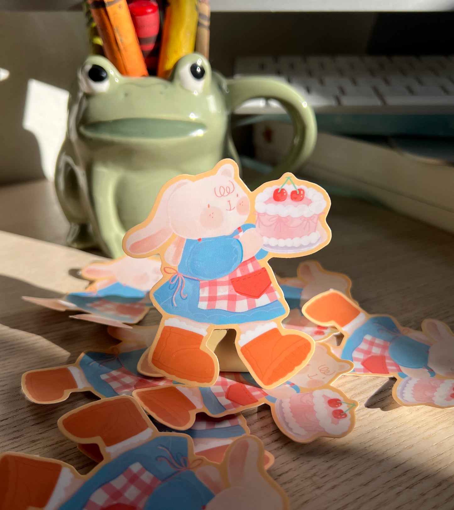 Cartoon Bunny stickers on a wooden desk with crayons in a frog shaped mug in the background